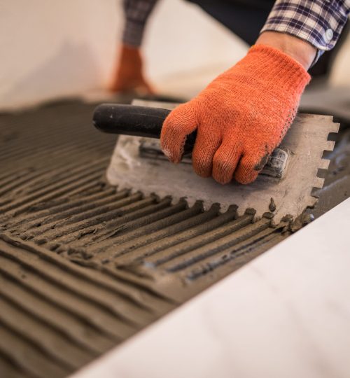 Troweling mortar onto a concrete floor in preparation for laying white floor tile.